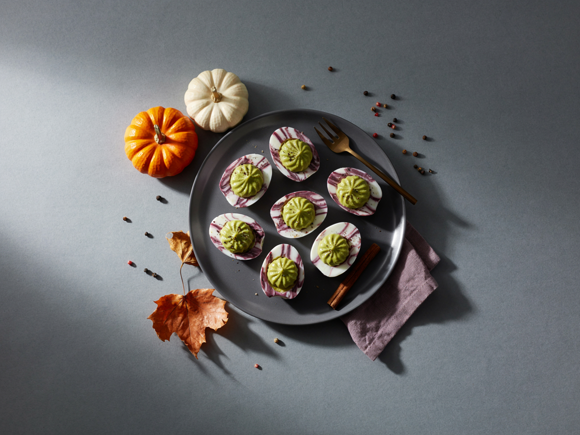 Spooky Halloween deviled eggs with purple marble-effect whites and green avocado filling piped in swirls on a dark plate