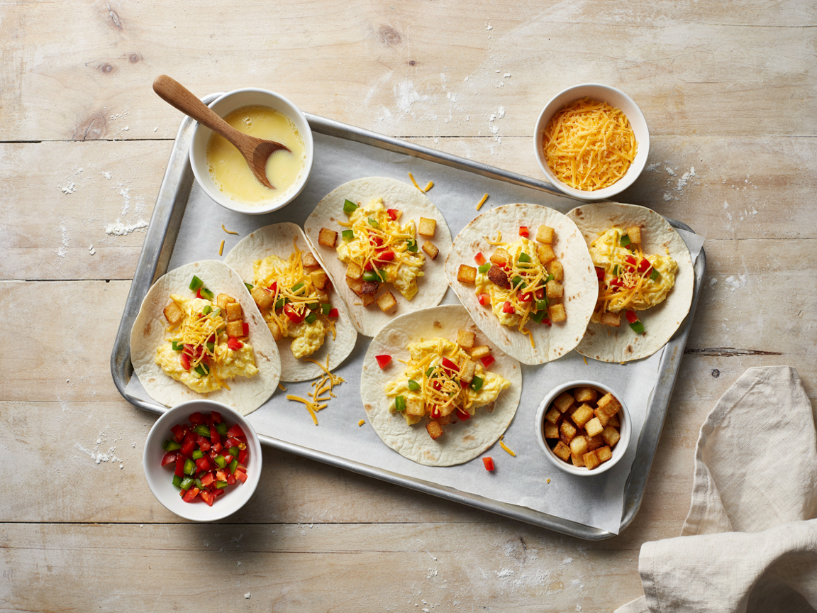Parchment-lined sheet pan with tortillas laid out and fillings ready to assemble breakfast burritos