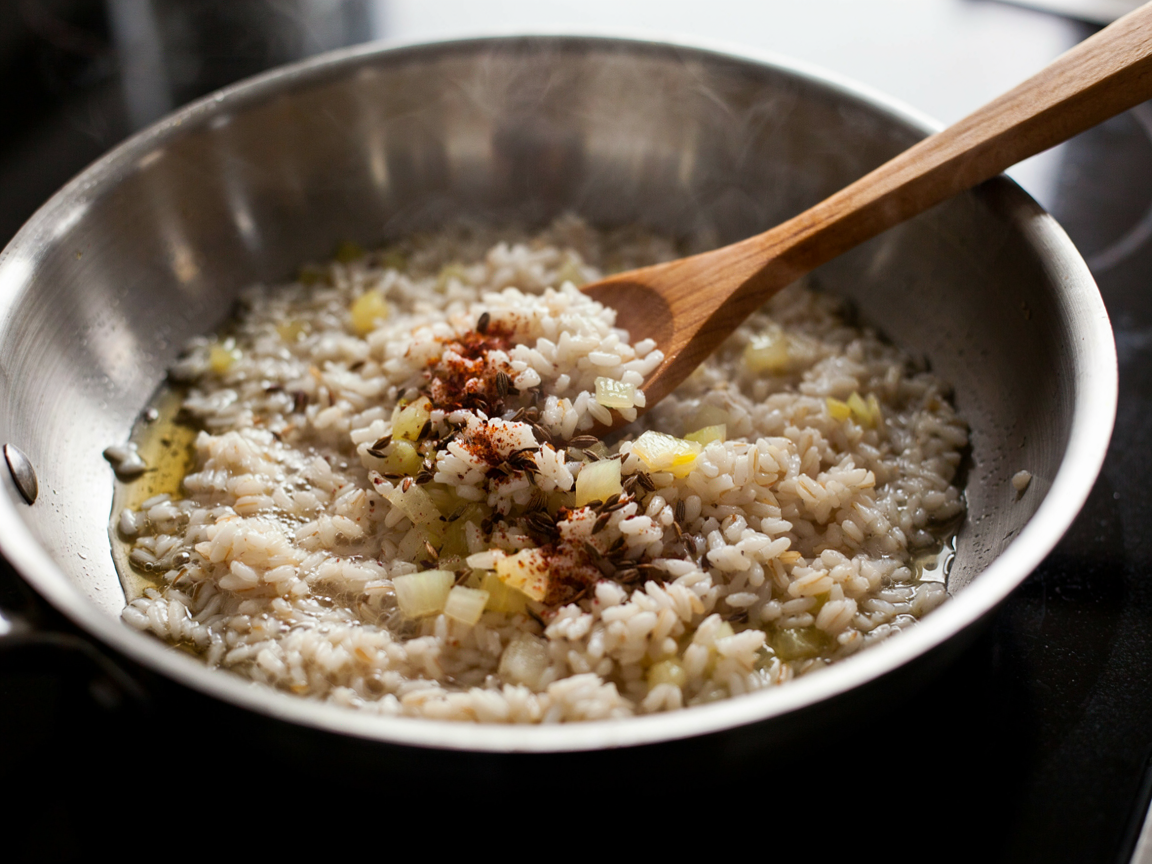 Long grain rice being toasted in oil in a skillet with diced onion, the grains turning chalky white