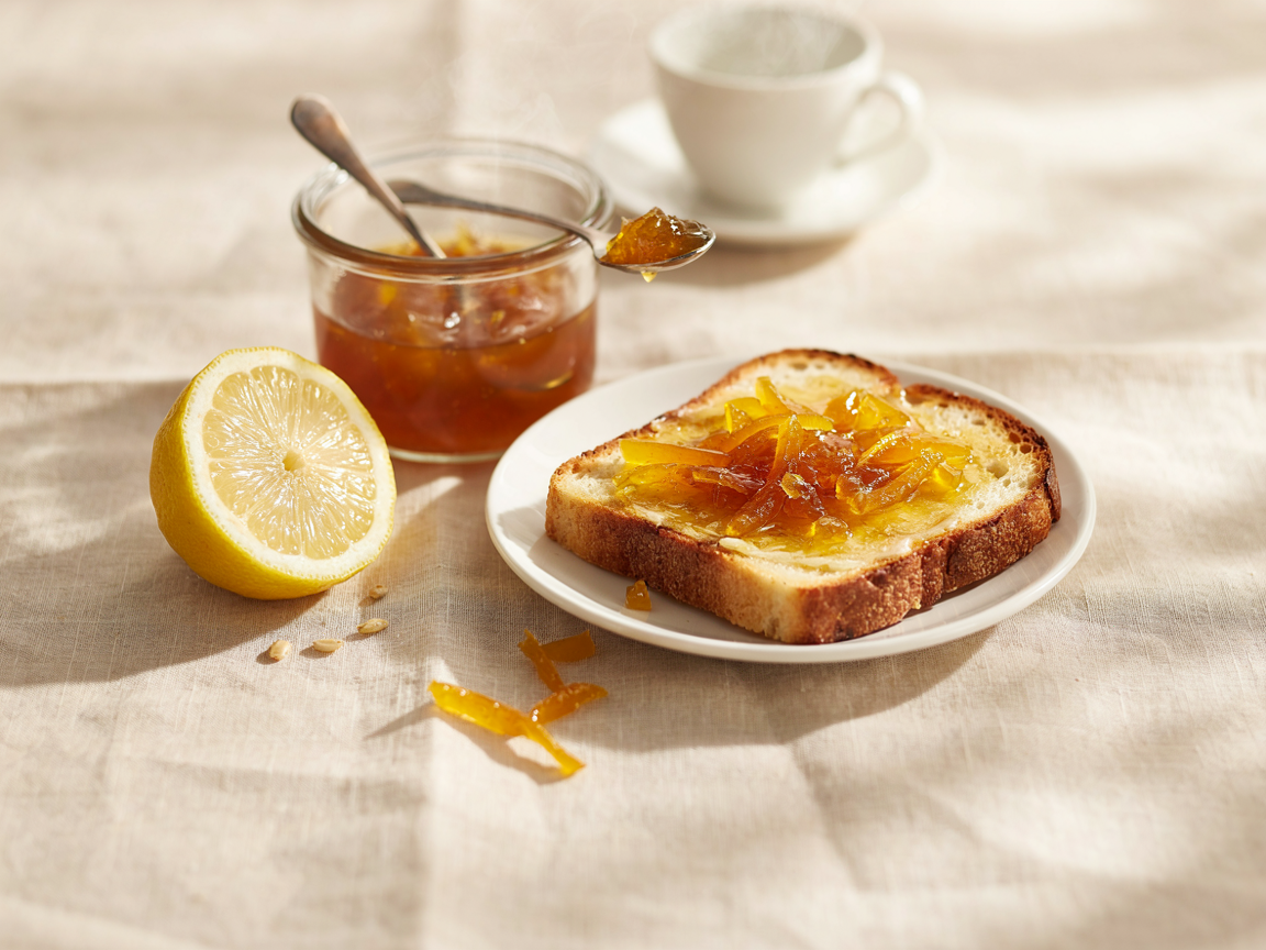 Lemon marmalade spread thickly on a slice of buttered toast on a small plate, with an open jar beside it
