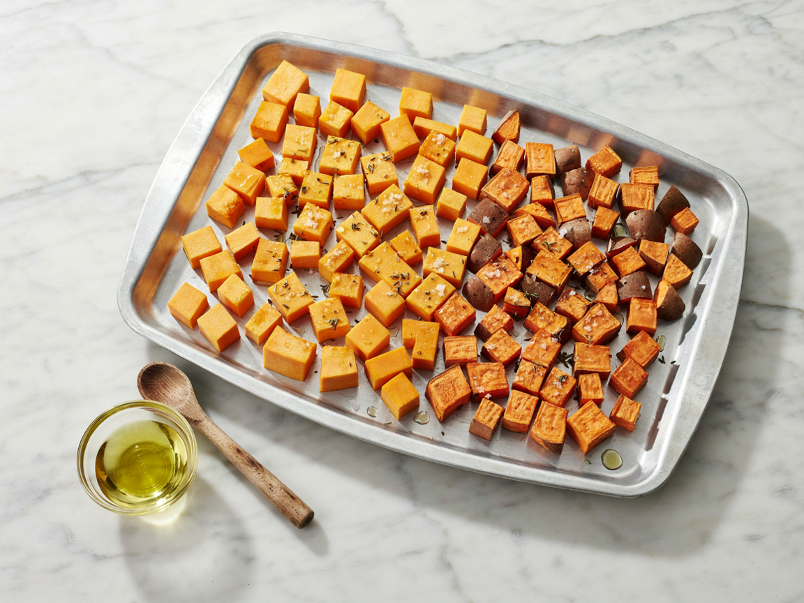 Raw cubed butternut squash and sweet potato tossed in olive oil and seasoning spread in a single layer on a sheet pan