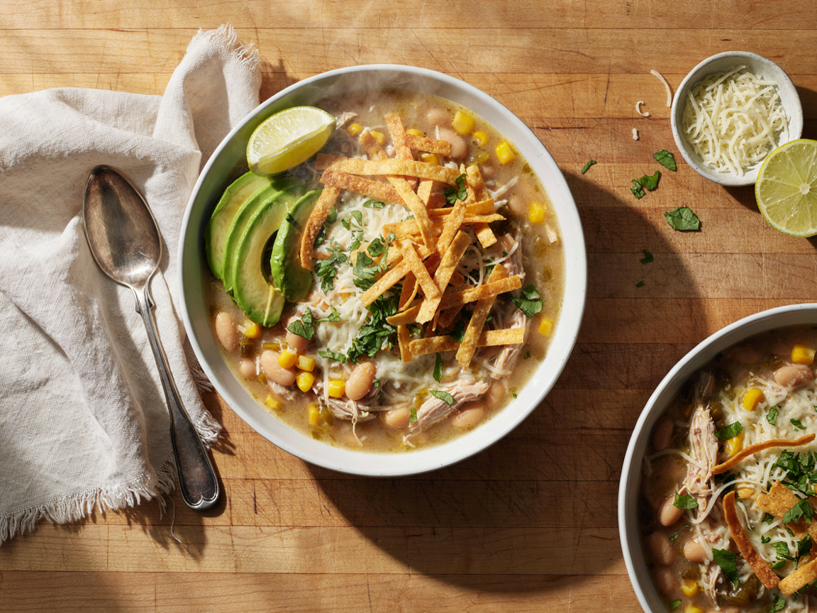 Creamy Instant Pot white chicken chili in a bowl with shredded chicken, white beans, corn, melted cheese, cilantro and tortilla strips