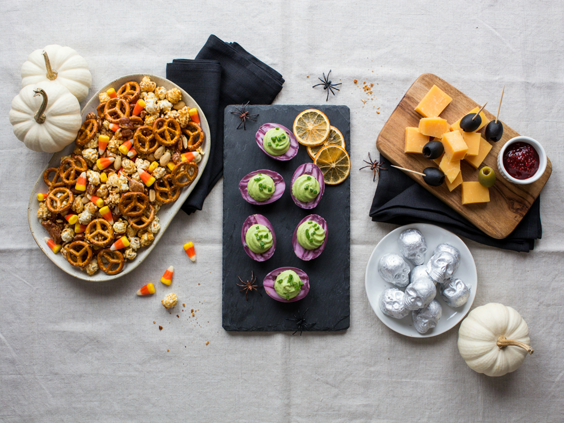 Halloween snack table with a platter of marbled deviled eggs, a witch hat cheese board, snack mix and skull truffles