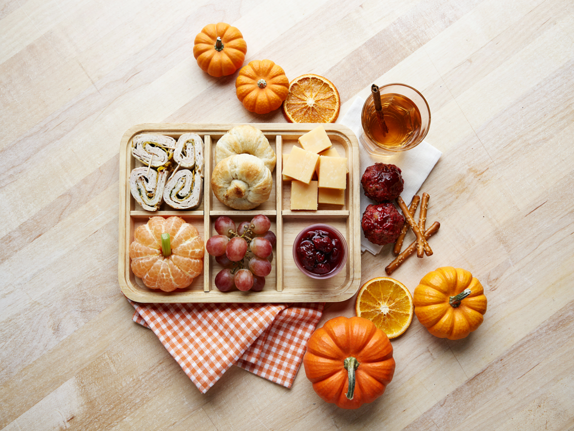 Thanksgiving kids lunch tray with turkey and cheese roll-ups, mini crescent rolls, cheese cubes, clementine segments, grapes and cranberry sauce