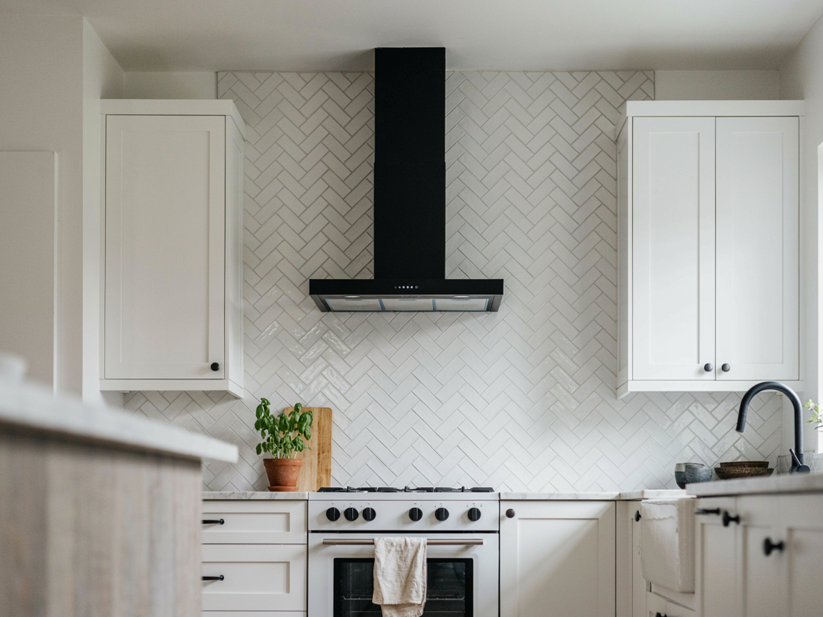 White kitchen with a matte black wall mount chimney range hood, white herringbone tile and black hardware